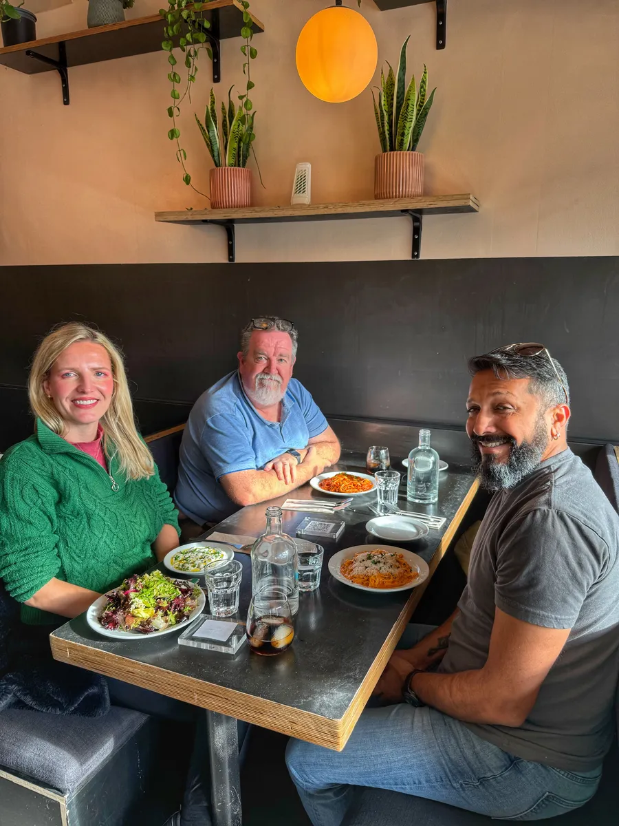 Three creative professionals enjoy lunch together at a Dublin restaurant with modern décor, plants, and warm lighting.