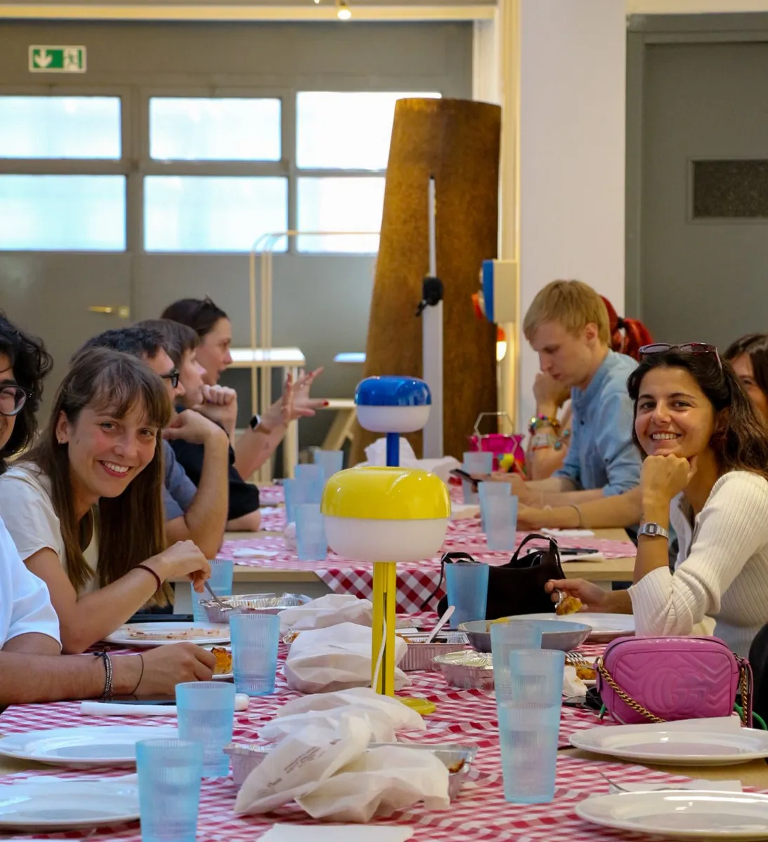 Group of young professionals smiling at a pink-themed lunch table during a Creative Lunch Club meetup in Milan.