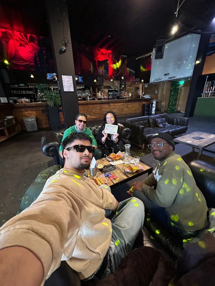 Group of five people at a Creative Lunch Club meetup in a London venue with red lighting and lounge seating, enjoying food and drinks.