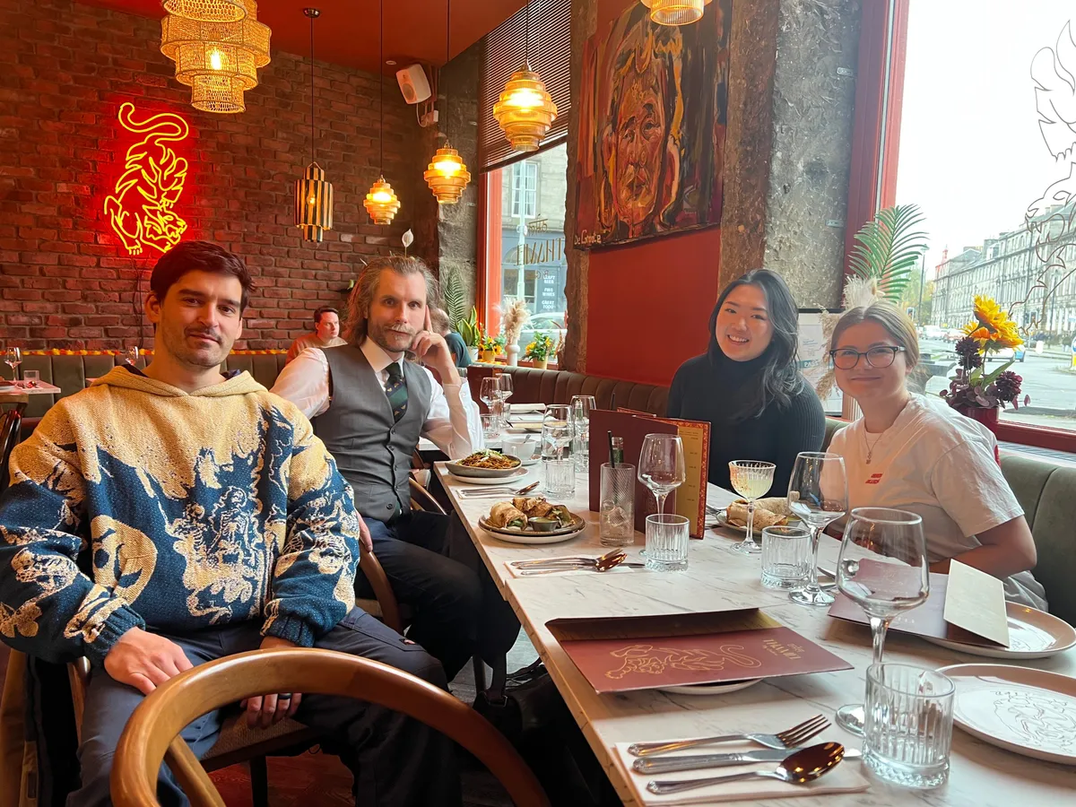 Four creative professionals dining together at an upscale Edinburgh restaurant with red brick walls and golden lighting fixtures.