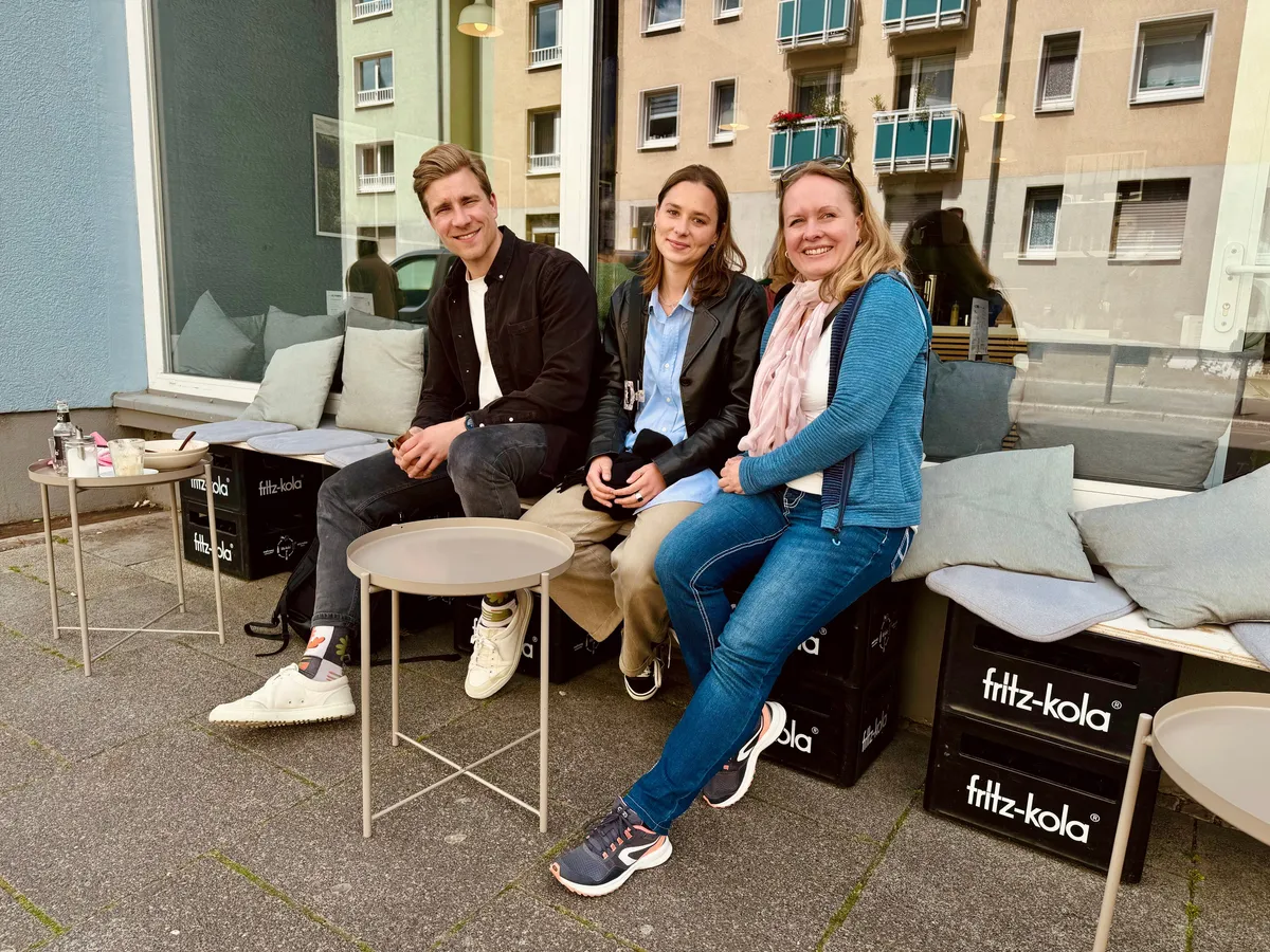 Three creative professionals sitting on black ottomans at a Frankfurt outdoor patio during a Creative Lunch Club meetup.