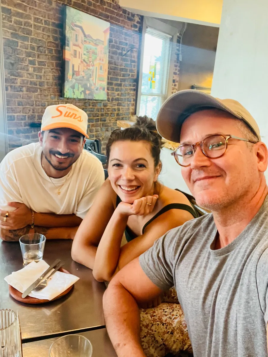 Three smiling people at a Creative Lunch Club meetup in Washington, posing together at a table in a brick-walled restaurant.