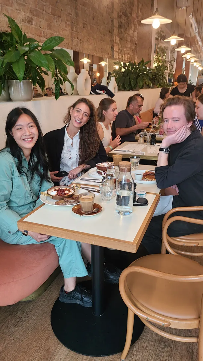 Group of creative professionals enjoying lunch together at a modern brick restaurant with plants and pendant lighting in London.
