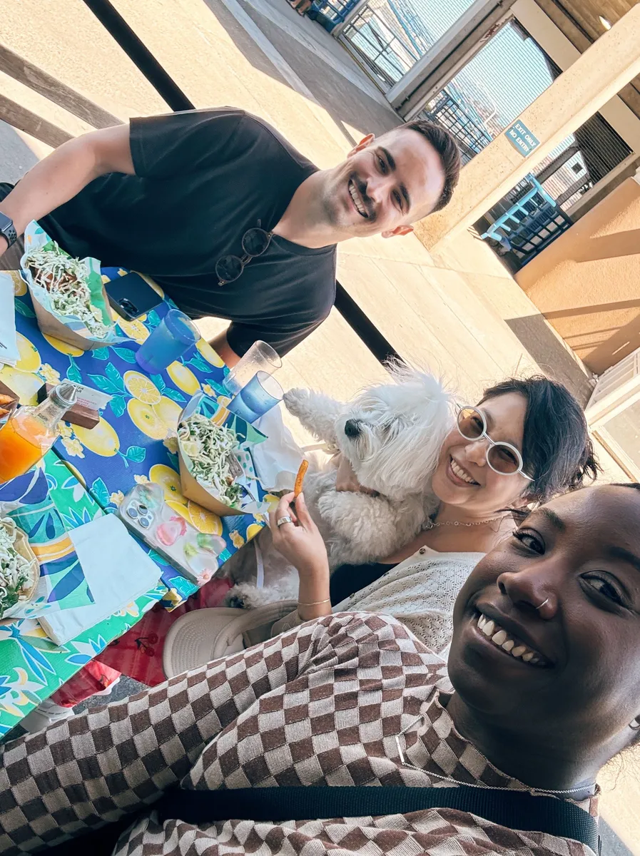 Three people and a small white dog enjoying lunch outdoors in San Francisco during a Creative Lunch Club meetup.