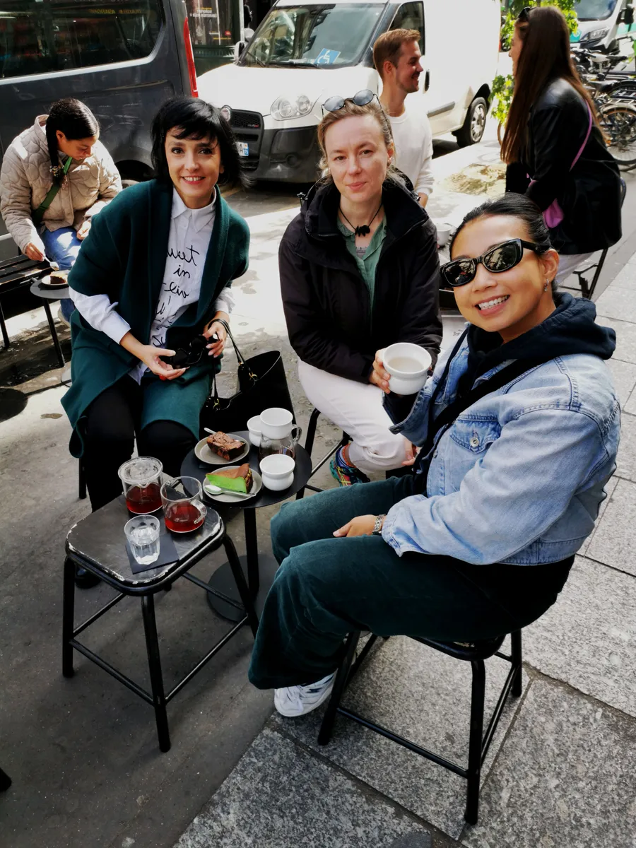 Four young people sitting outdoors in Paris enjoying drinks and snacks at a Creative Lunch Club meetup in an urban setting.