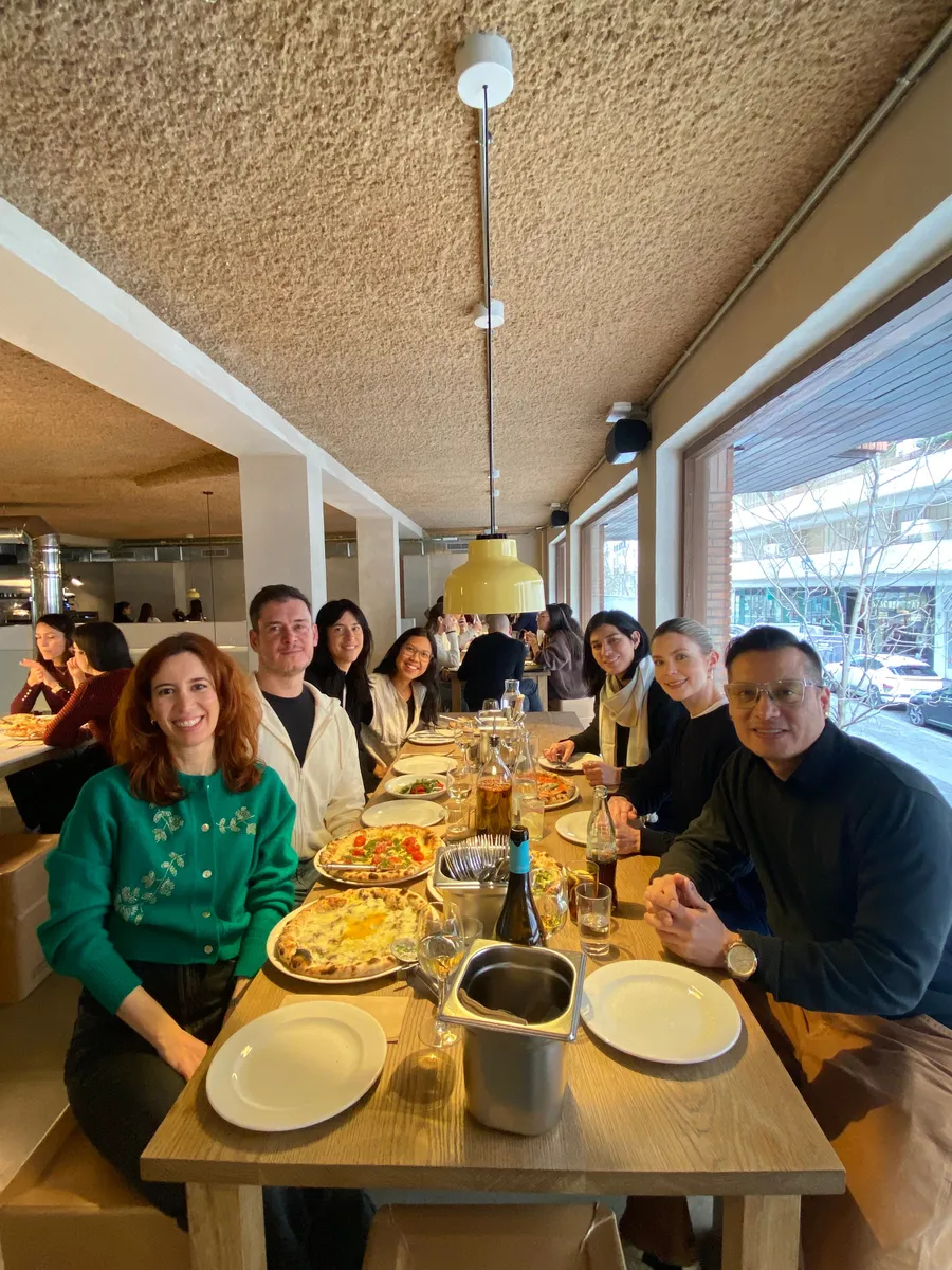 Group of creative professionals dining together at a Creative Lunch Club meetup in Madrid, seated at a long wooden table with food and drinks.