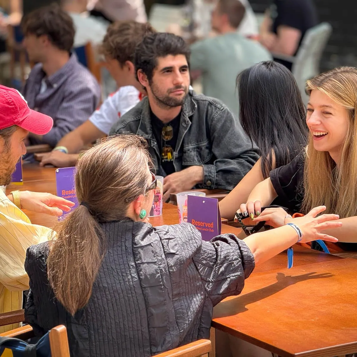 People socializing at a Creative Lunch Club meetup, seated at a wooden table with purple reserved cards.