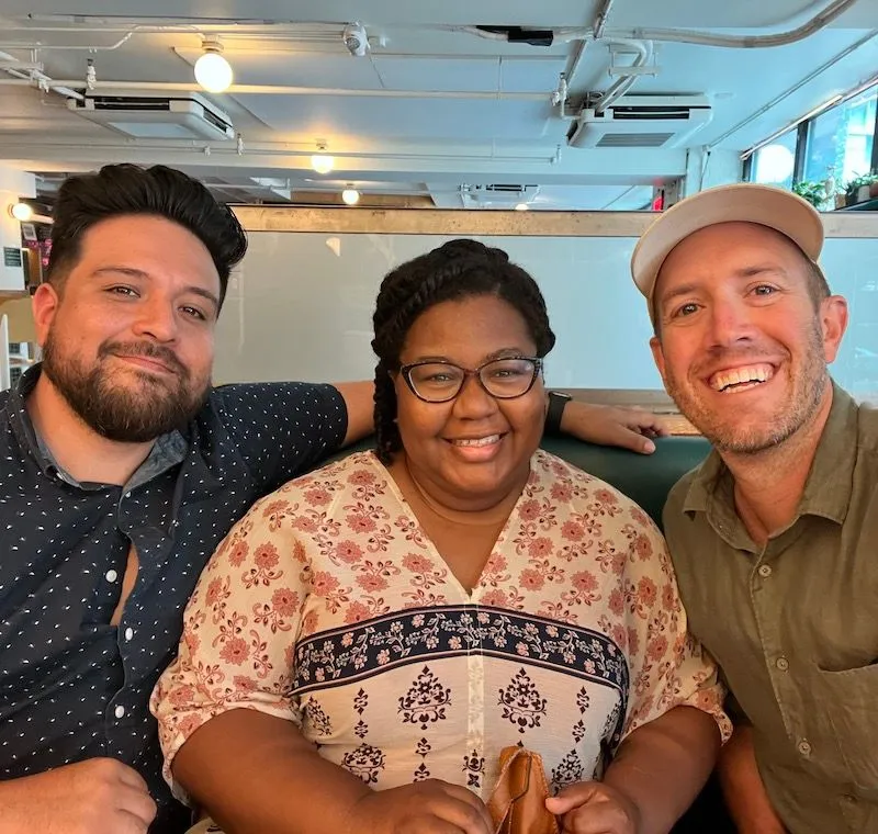 Three smiling people posing together at a Creative Lunch Club meetup in Philadelphia, indoors with modern ceiling fixtures.