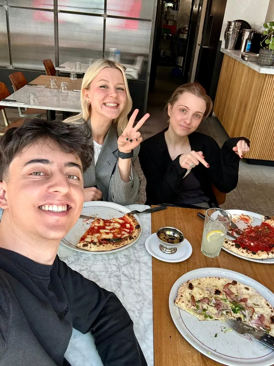 Three young professionals smiling at a pizza restaurant table in Warsaw during a Creative Lunch Club meetup event.