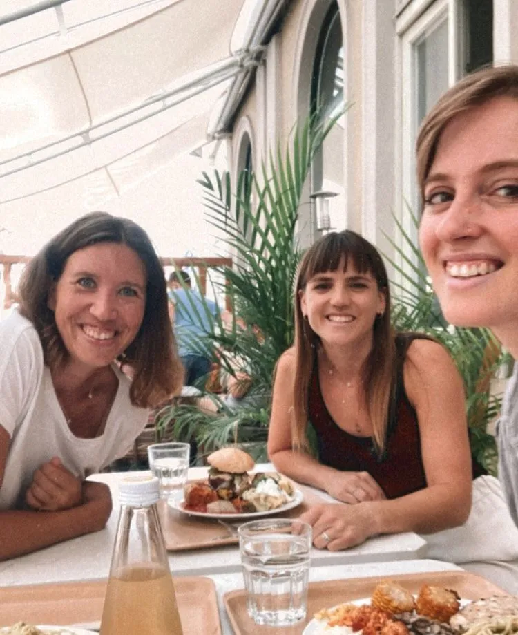 Three smiling women dining together at a bright, plant-filled indoor venue during a Creative Lunch Club meetup in Graz.