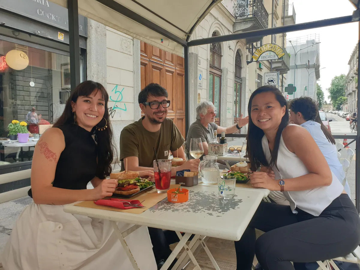 Four people enjoying lunch at an outdoor café table in Turin, smiling at the camera during a Creative Lunch Club meetup.