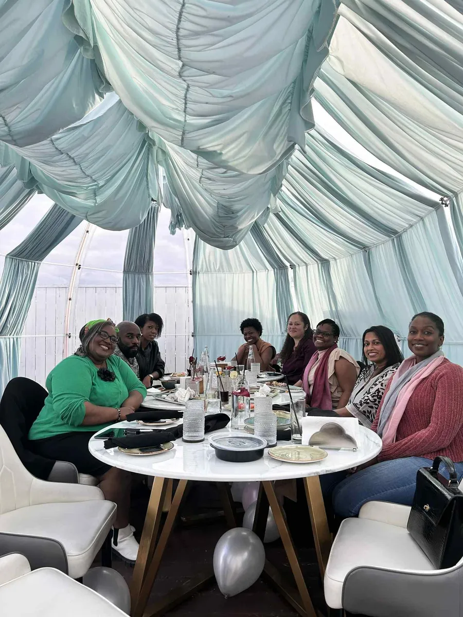 Group of diverse creative professionals gathered around a white round table in a light blue tent for a Creative Lunch Club meetup in Toronto.