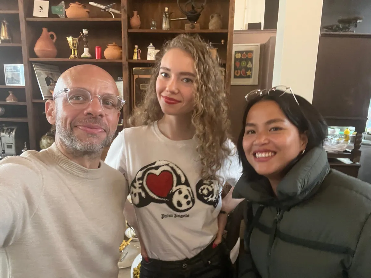 Three people smiling at a Creative Lunch Club meetup in Geneva, standing in front of shelves with decorative items and collectibles.