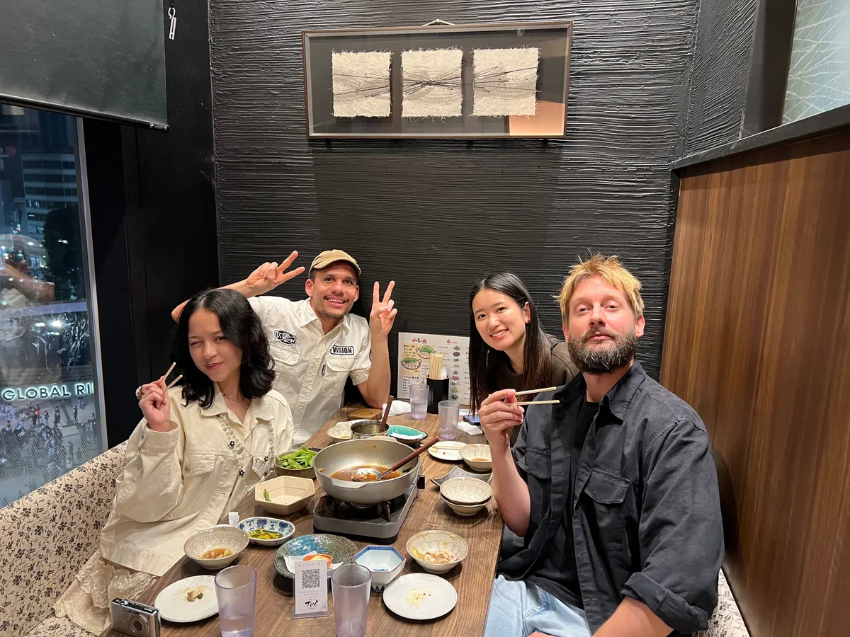 Five people enjoying a hotpot meal together at a Creative Lunch Club meetup in Tokyo, smiling at the camera with chopsticks raised.